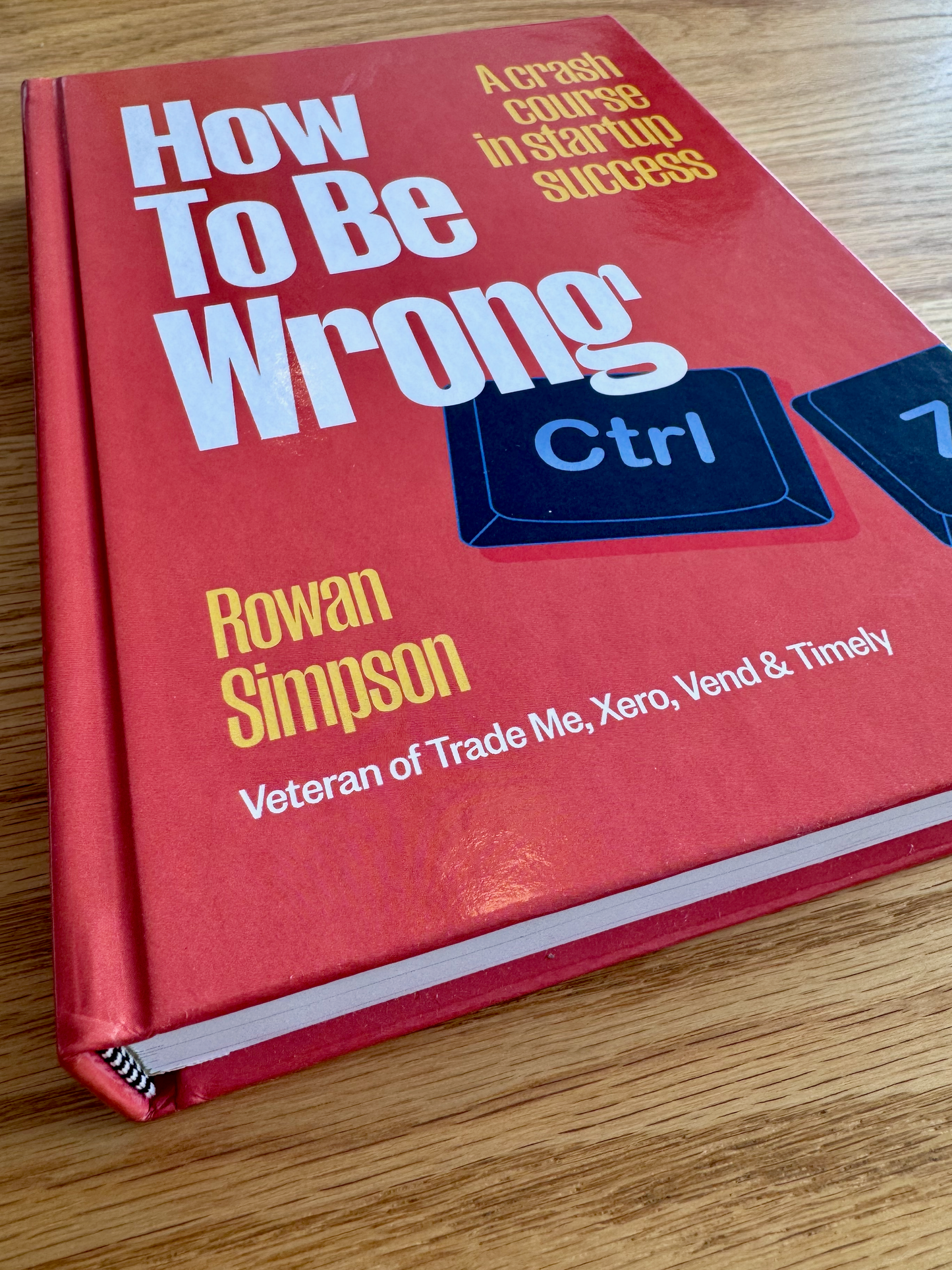 Book titled 'How To Be Wrong' by Rowan Simpson on a wooden surface