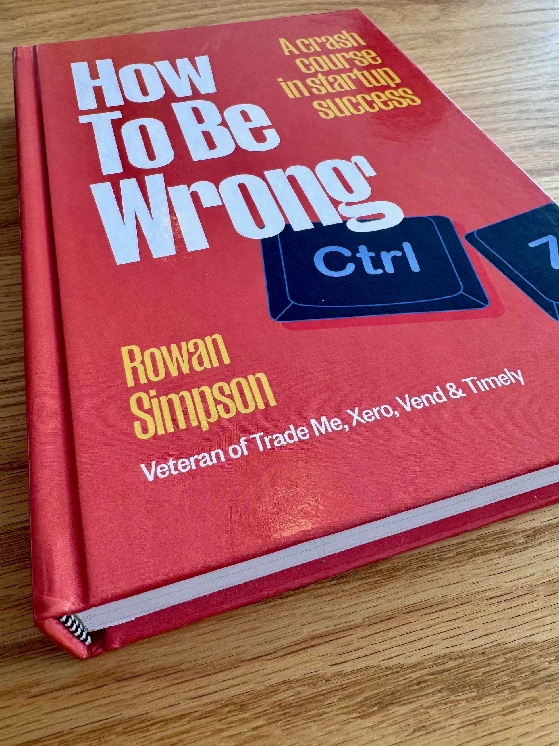 Book titled 'How To Be Wrong' by Rowan Simpson on a wooden surface